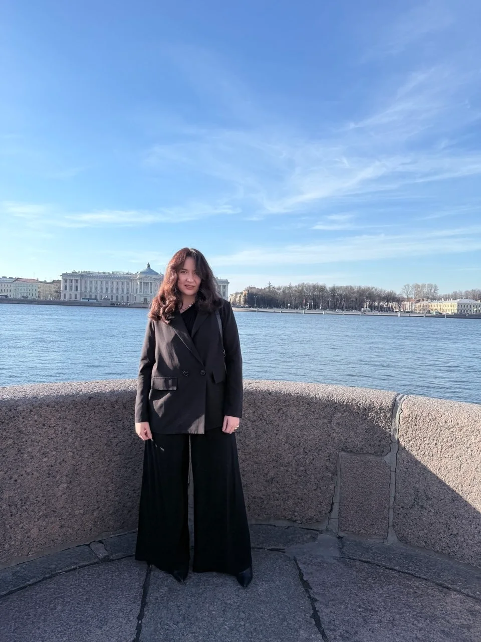 Dina Mi in a black suit beside the Neva River
